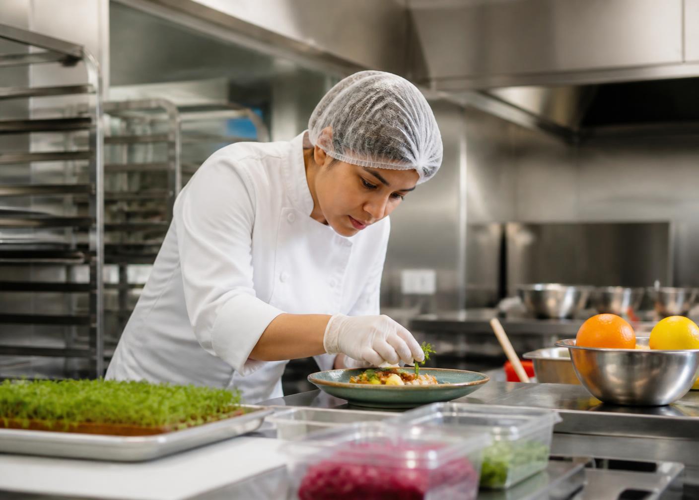 Profissional de cozinha finalizando prato em cozinha industrial organizada e higienizada